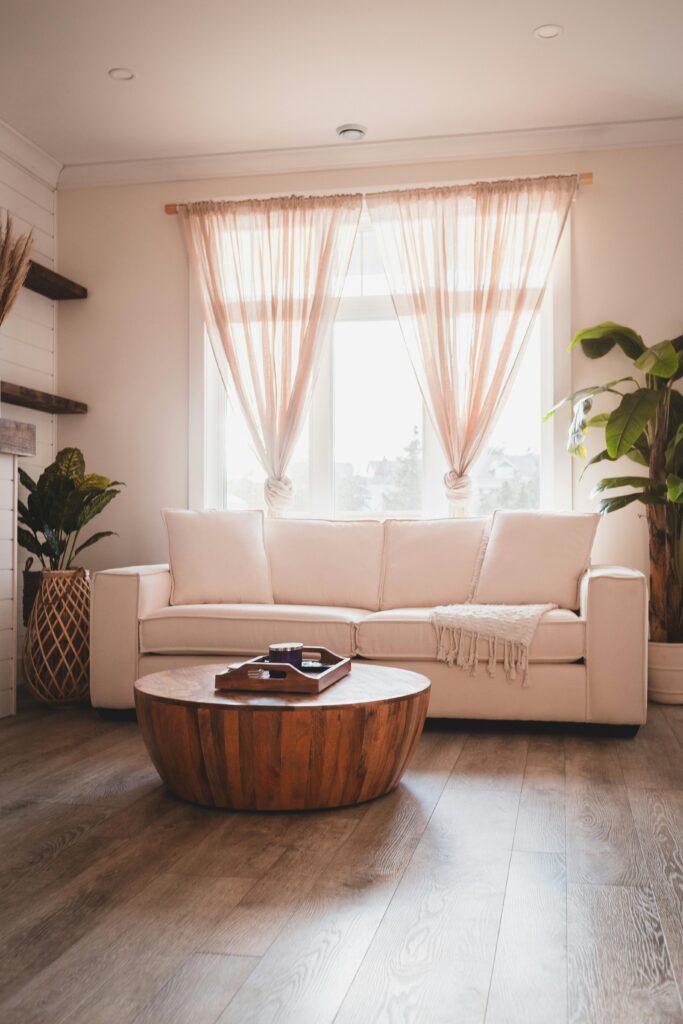 Bright and stylish living room interior with beige couch, wooden table, and sunlight streaming through sheer curtains.