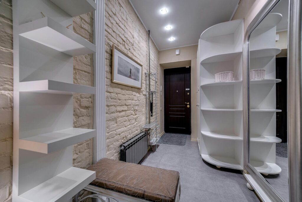 Contemporary entryway with sleek white shelving and neutral tones, featuring a comfortable bench.