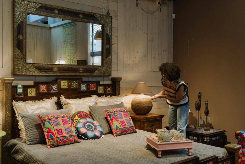 Elegant bedroom featuring colorful bohemian decor and a woman setting up a lamp.
